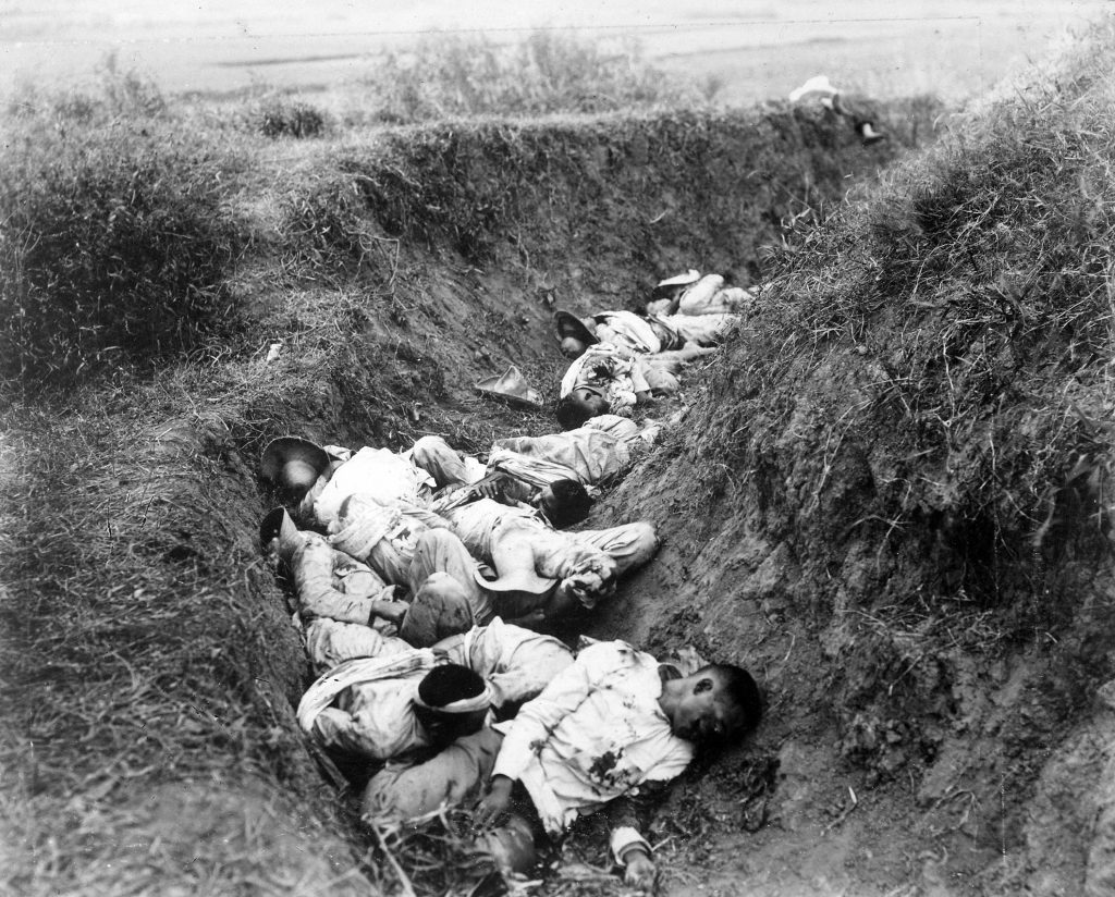 Many Filipino soldiers lying dead in a circular trench. Only a small portion of the trench is shown in this photo but the trench's actual size is much larger.
