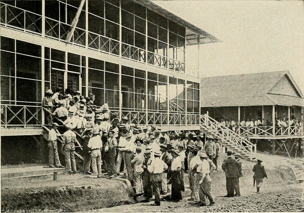 A black and white photo of Panama Canal workers entering a building in a large group.
